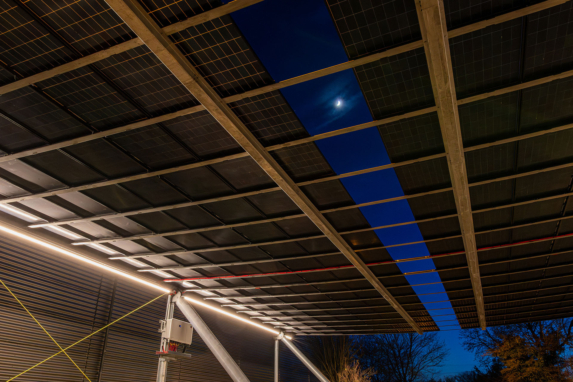 Blick auf den beleuchteten Parkplatz unter der Photovoltaikanlage in Hemmingen am Abend, Photovoltaik Parkplatzüberdachung Hemmingen mit Solarmodulen und Blick auf Stellplätze